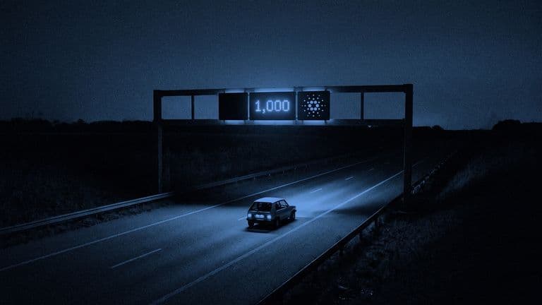 A road gantry with a display reading 1,000 and the Cardano mark hangs over an empty lane with one small car beneath it.