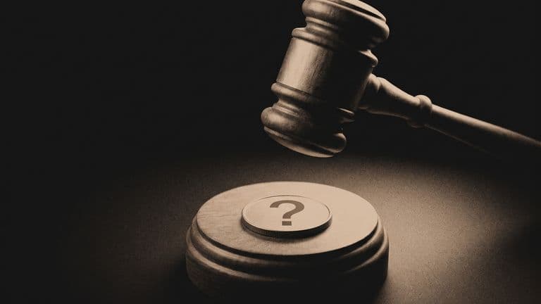 A wooden gavel raised above a plain coin marked with a question mark.