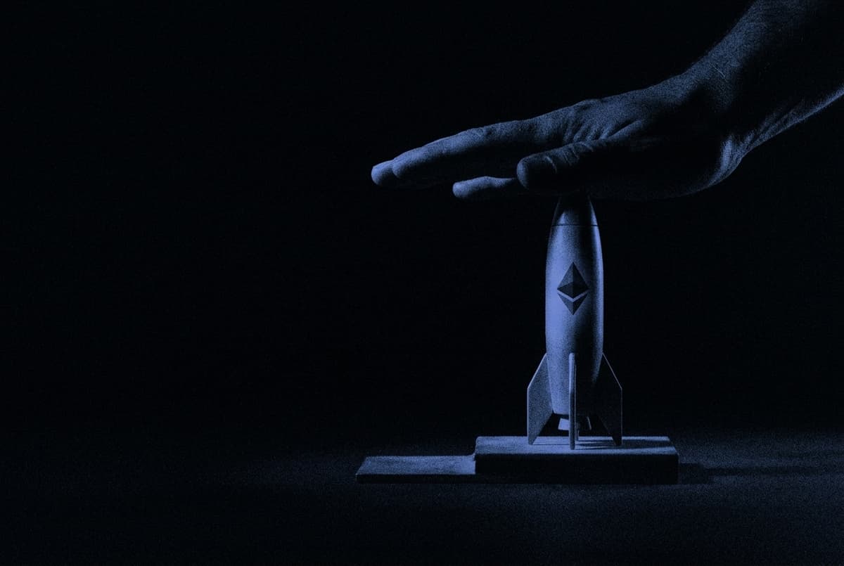 A giant hand presses down on the nose of a small rocket marked with the Ethereum logo, holding it on its launch pad in the dark.