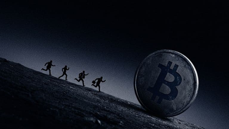 A giant Bitcoin coin rolls down a dark slope while a few small suited figures run downhill after it.