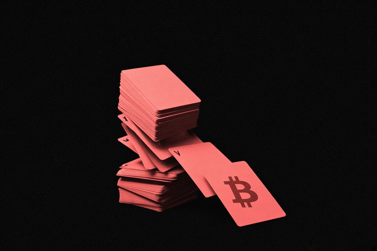A house of playing cards collapsing in the dark, the top card with the Bitcoin mark falling toward the viewer.