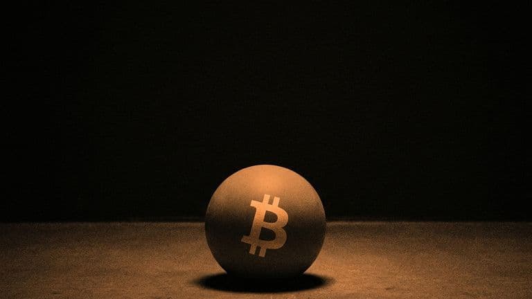 A ball bearing the Bitcoin mark, caught at the moment it strikes a hard floor in a dark empty space.