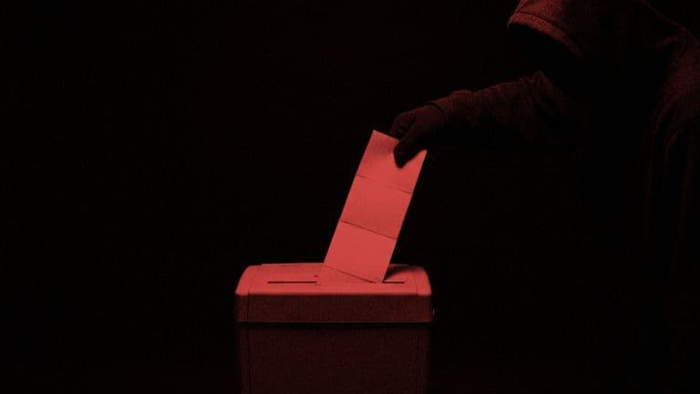 A paper shredder has failed to cut a stack of shipping labels, and a giant hooded hand is pulling them out of its slot.