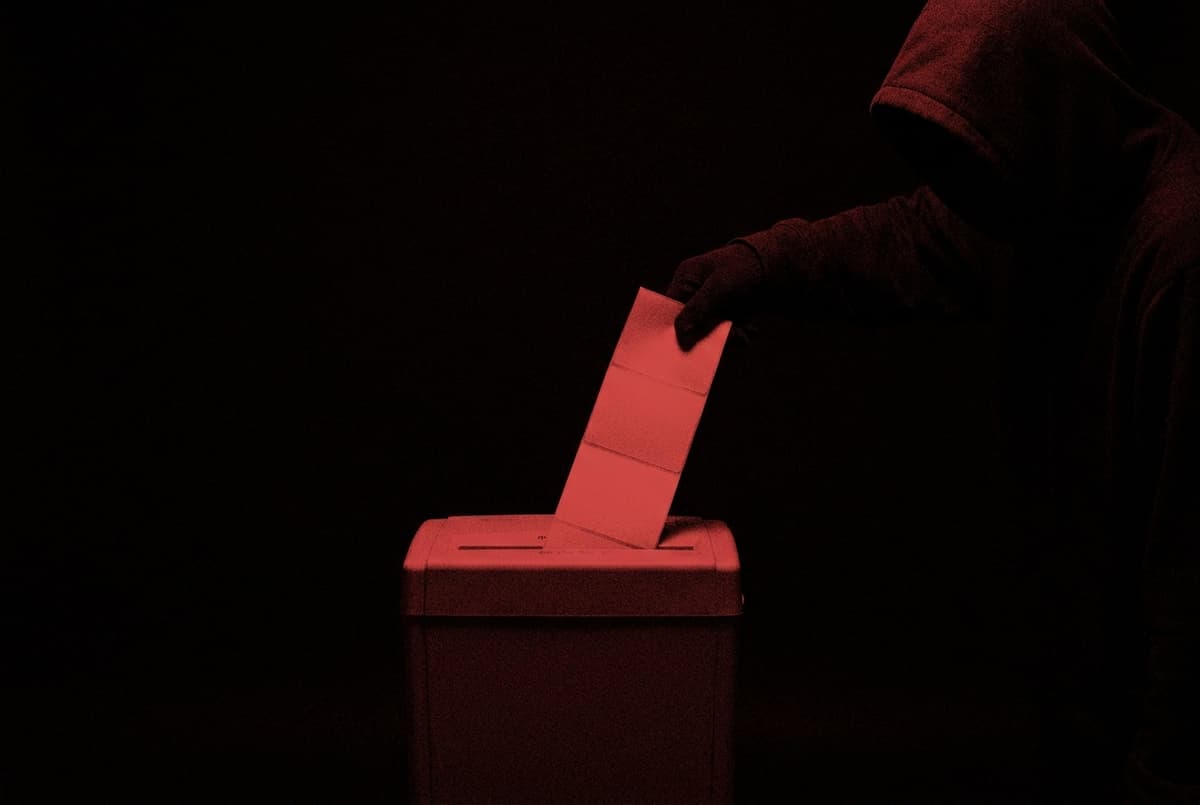 A paper shredder has failed to cut a stack of shipping labels, and a giant hooded hand is pulling them out of its slot.